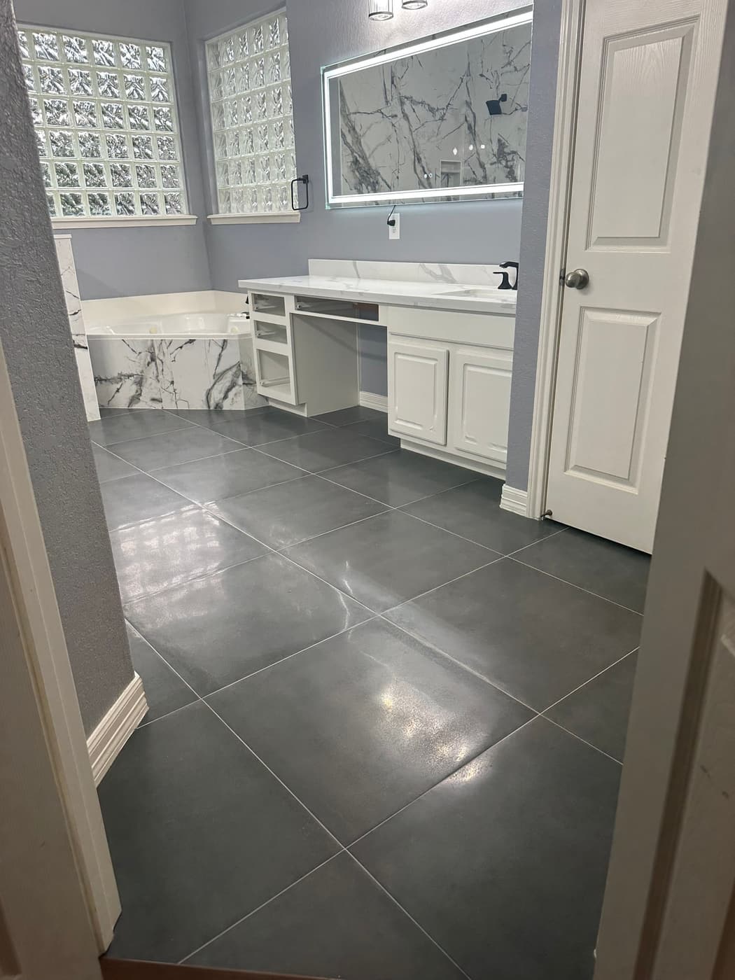 Remodeled bathroom with gray porcelain floor tile laid diagonally, white vanity and marble-look accents