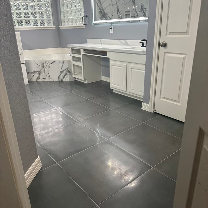Remodeled bathroom with gray porcelain floor tile laid diagonally, white vanity and marble-look accents