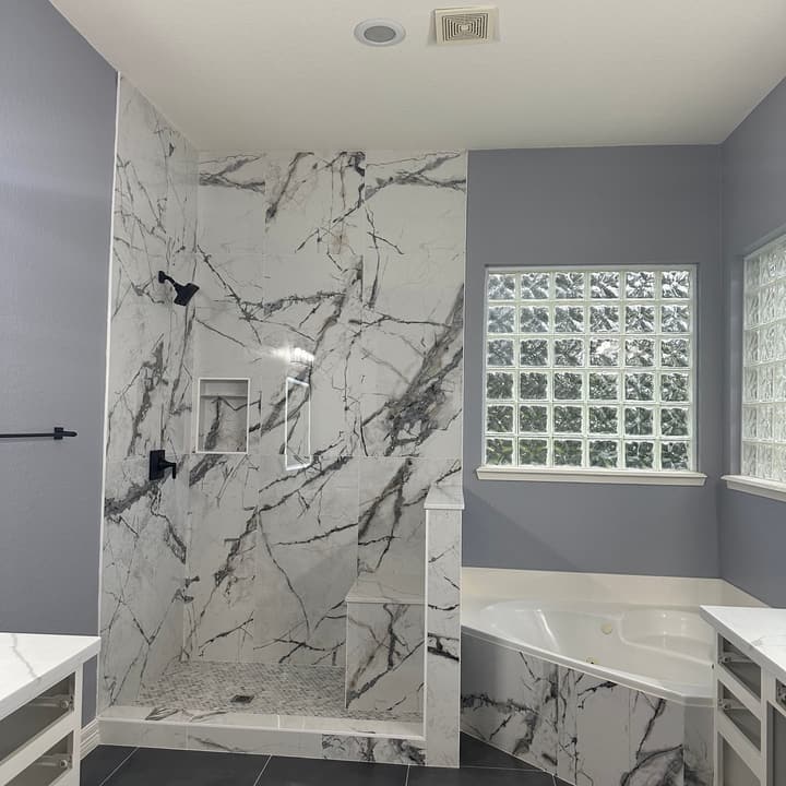 Walk-in shower in large-format marble-look wall tile with a tiled niche and black fixtures