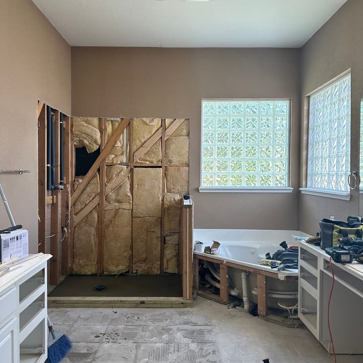 Bathroom mid-remodel with wall framing and insulation exposed and the old tile floor removed