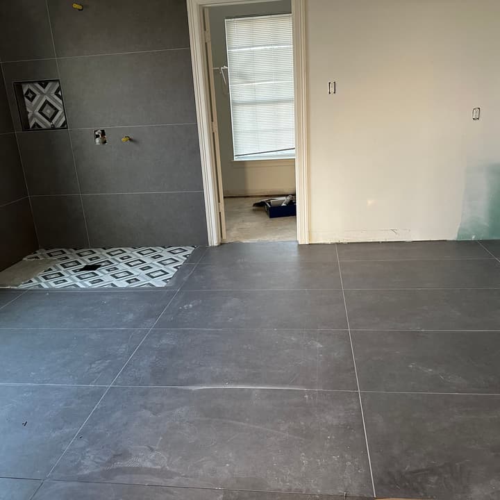 Shower walls in dark large-format tile with a patterned mosaic niche and shower pan in progress
