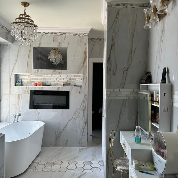 Master bathroom in marble-look tile with a freestanding tub, hexagon mosaic band and wall fireplace