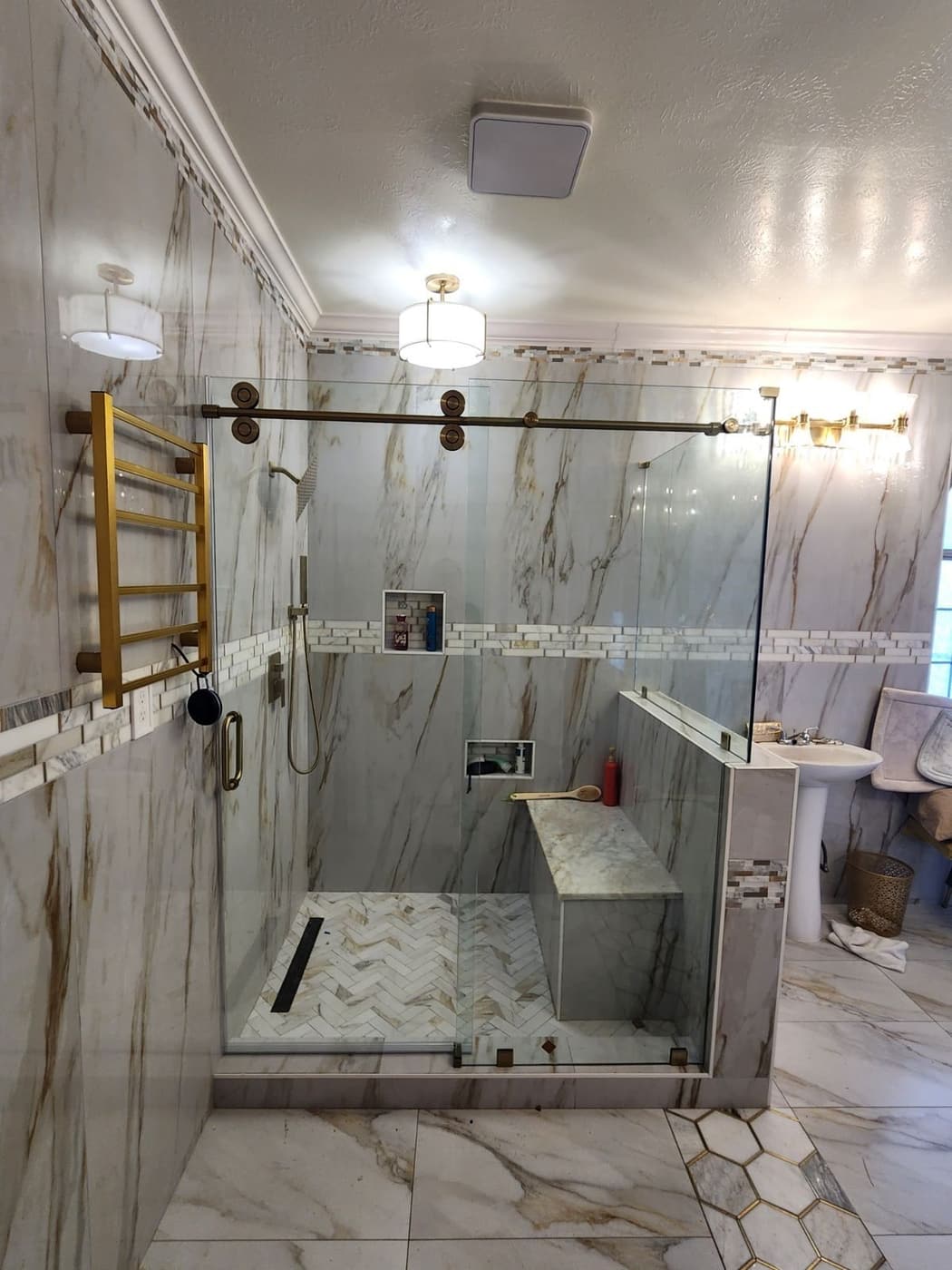 Walk-in shower with sliding glass door, brass hardware and a herringbone mosaic floor