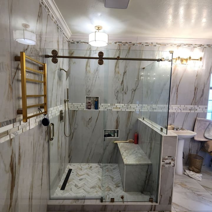Walk-in shower with sliding glass door, brass hardware and a herringbone mosaic floor