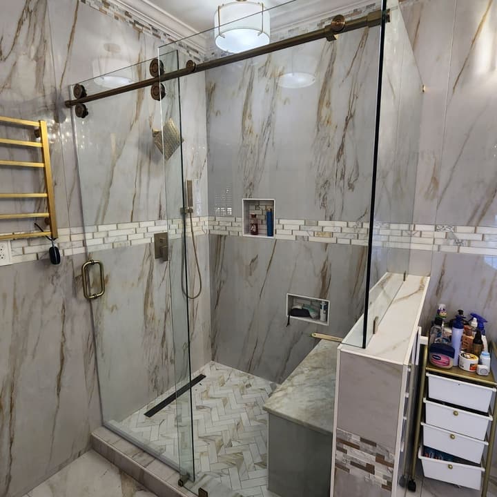 Shower in white subway tile with a marble hexagon mosaic pan, glass panel and black fixtures